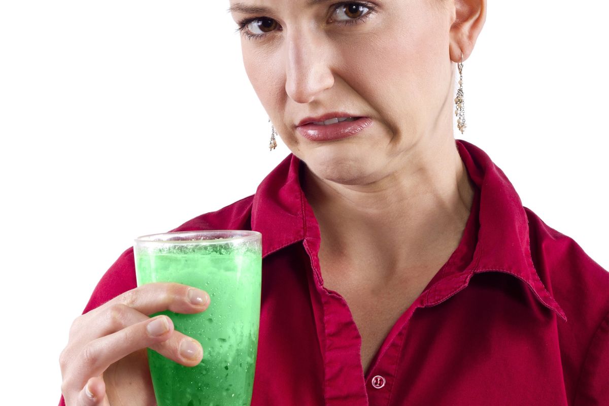 Woman looking grossed out drinking a green drink