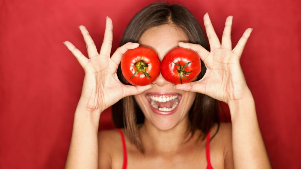 happy woman covering eyes with tomato