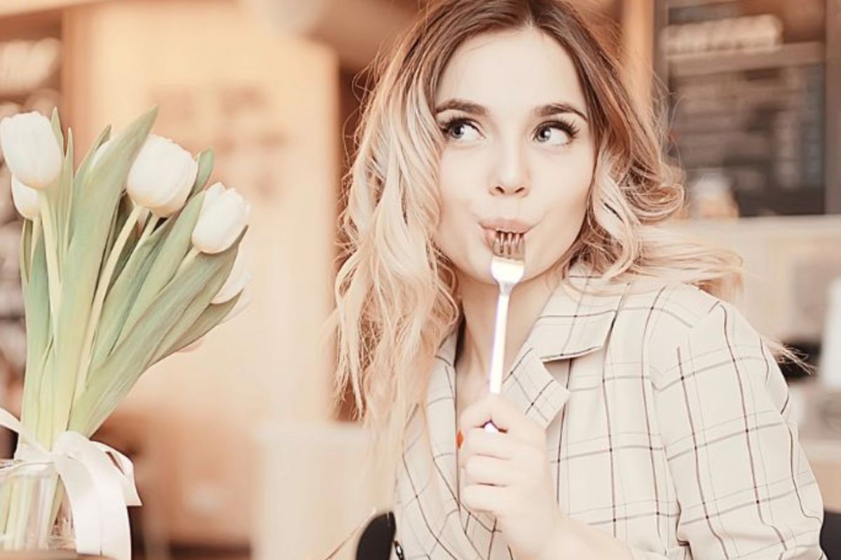 happy woman sitting with fork in mouth at table