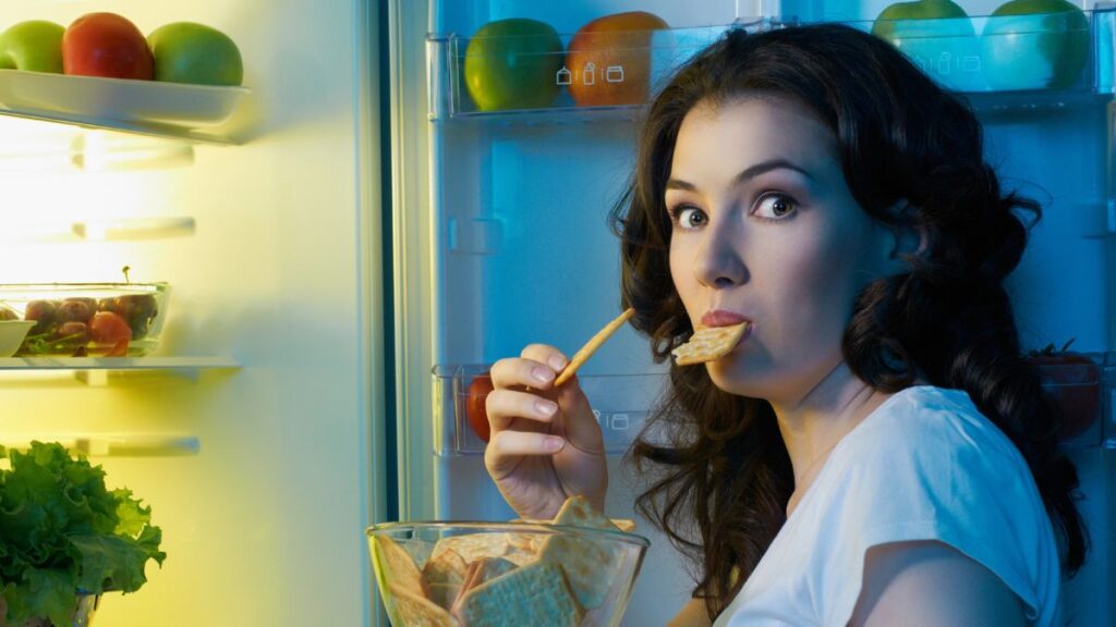 woman eating crackers in fridge looking surprised