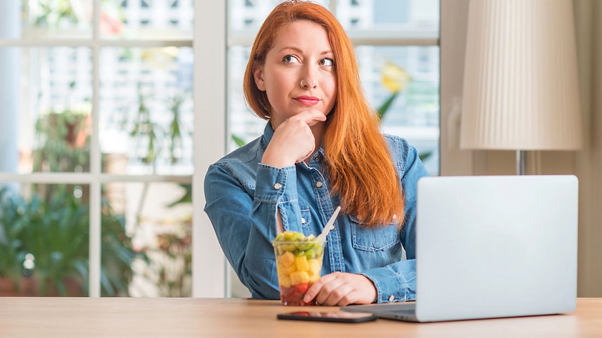 woman thinking with hand on chin and cup of fruit