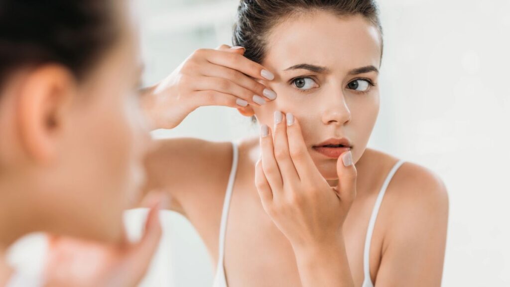 woman with acne looking in the mirror