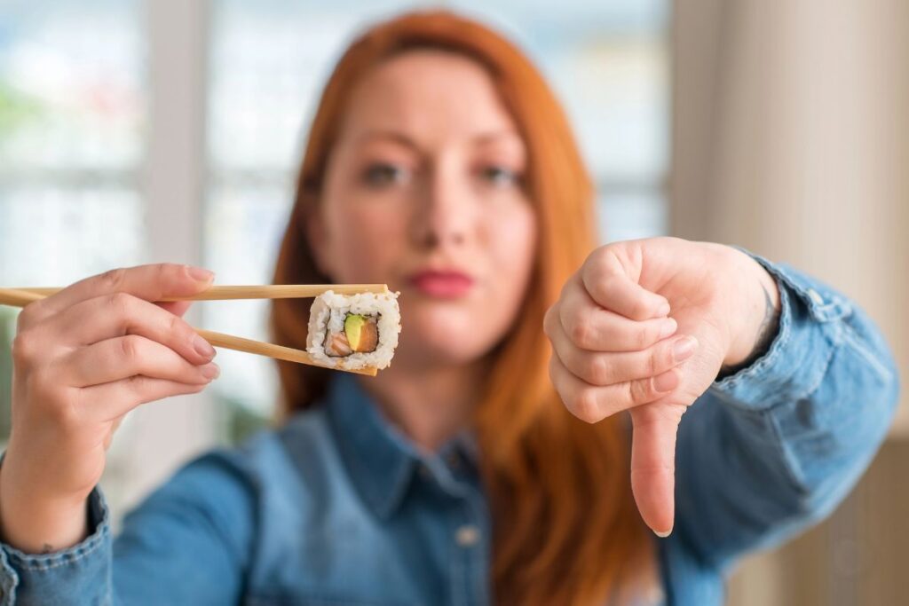 Woman holding a piece of sushi with her thumbs pointing down