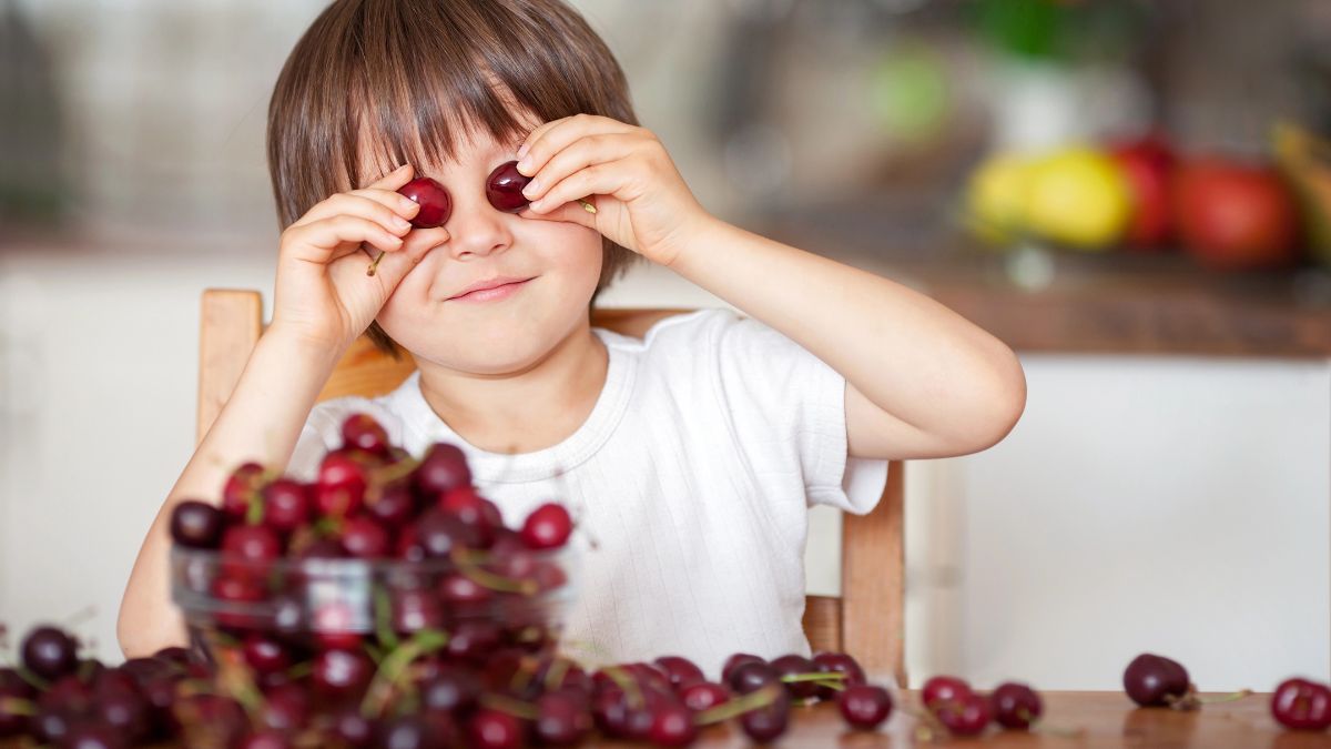 boy smiling with cherries holding 2 over eyes