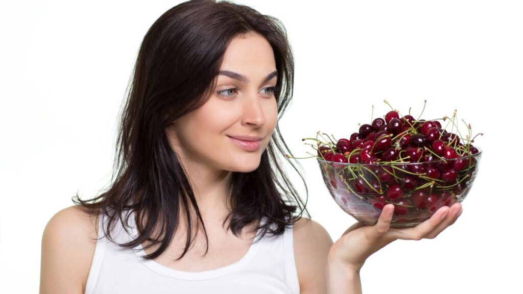 happy woman holding bowl of cherries in one hand