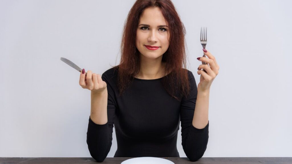 hungry woman waiting for food at table with empty plate