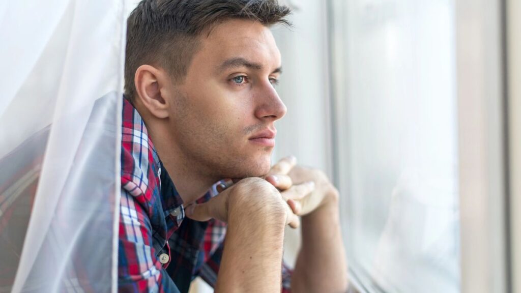 sad man looking out window with face on hands