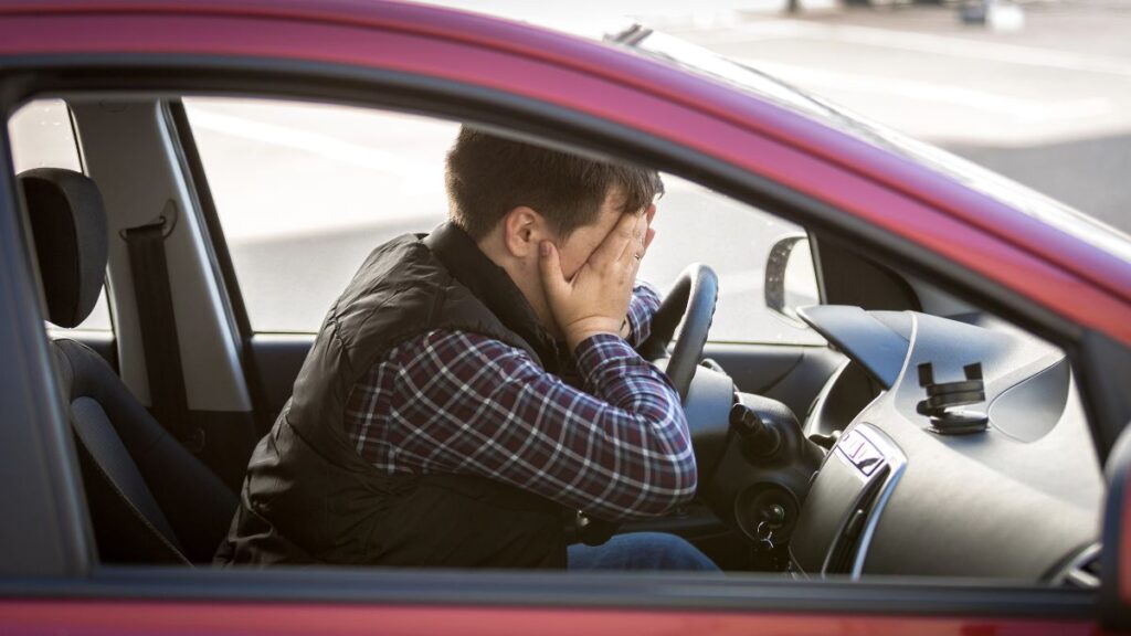 upset man covering face in drivers seat