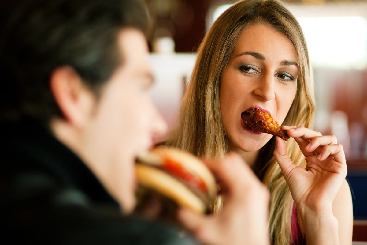 woman and man eating out, woman is mid bite of a wing