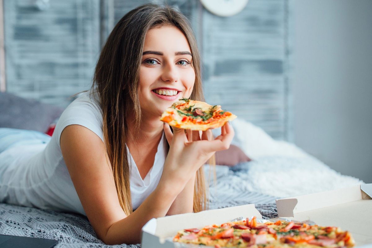 woman eating pizza in bed