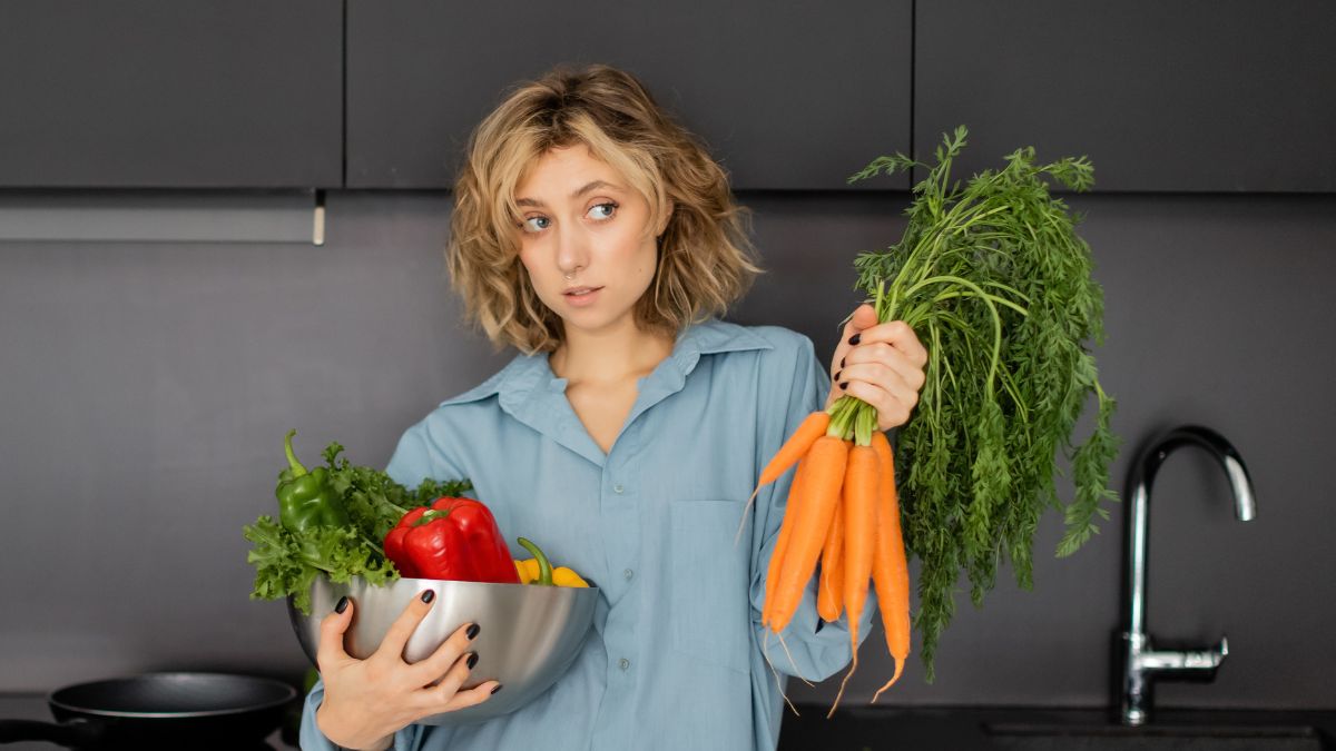 woman looking confused in the kitchen holding vegetables