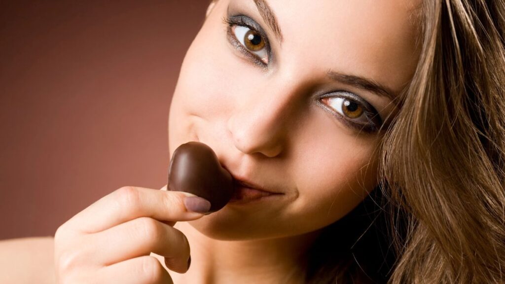 woman smiling with dark chocolate by mouth