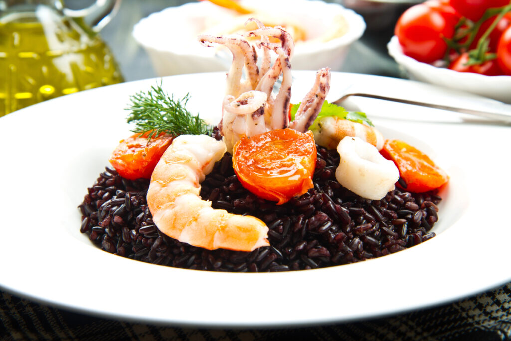 Black rice with sliced squids ,prawns and tomato on white plate