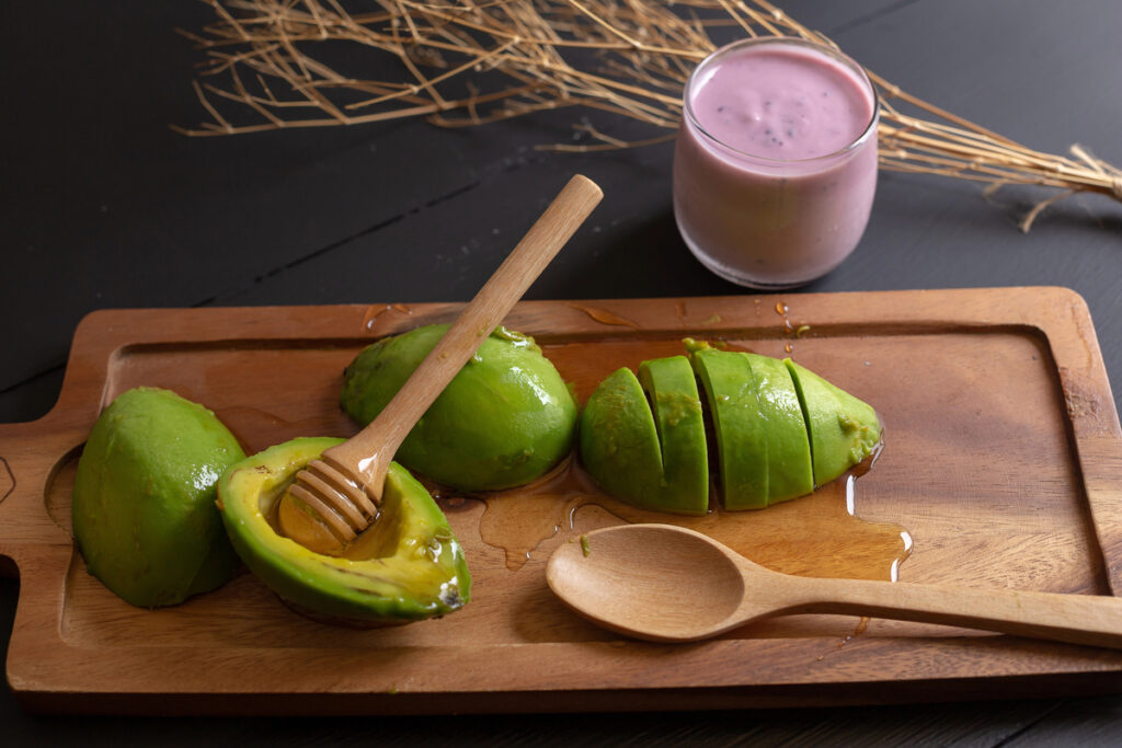 Fresh organic avocado sliced in half and honey on black wooden table.