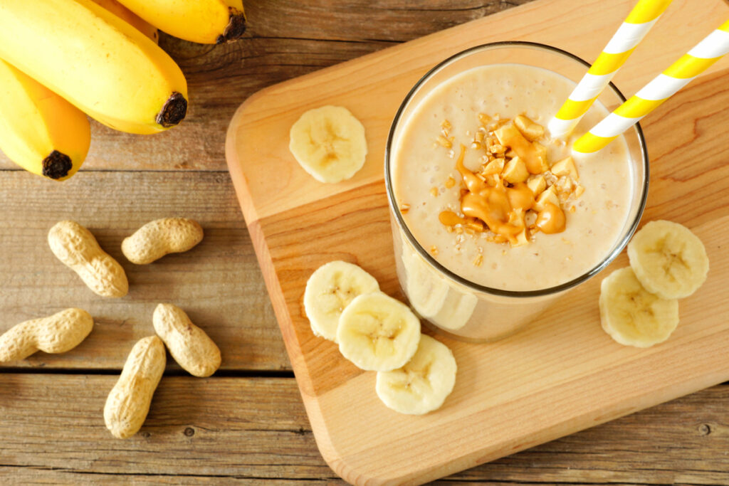 Peanut butter banana oat smoothie with paper straws, on a wood board on rustic table, downward view