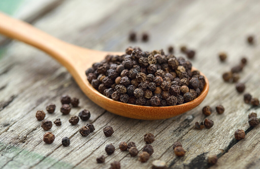 Whole black pepper on wooden spoon