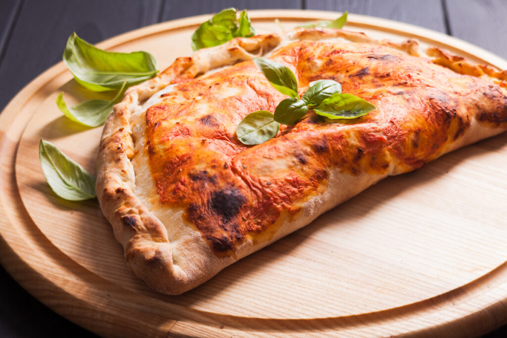 Pizza calzone with basil leaves close up