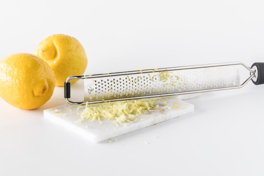 Lemon zest on a small marble slab with a microplane and two lemons to the left. Copy space above and below.