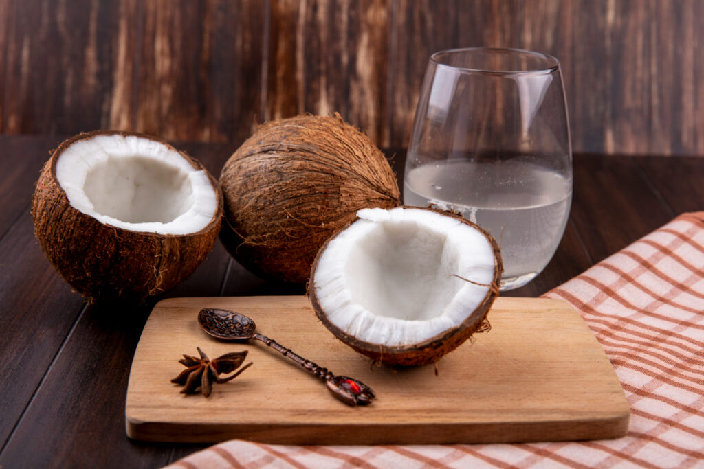 fresh coconuts on a wooden kitchen board with spoon and a glass of water on checked tablecloth and wooden surface