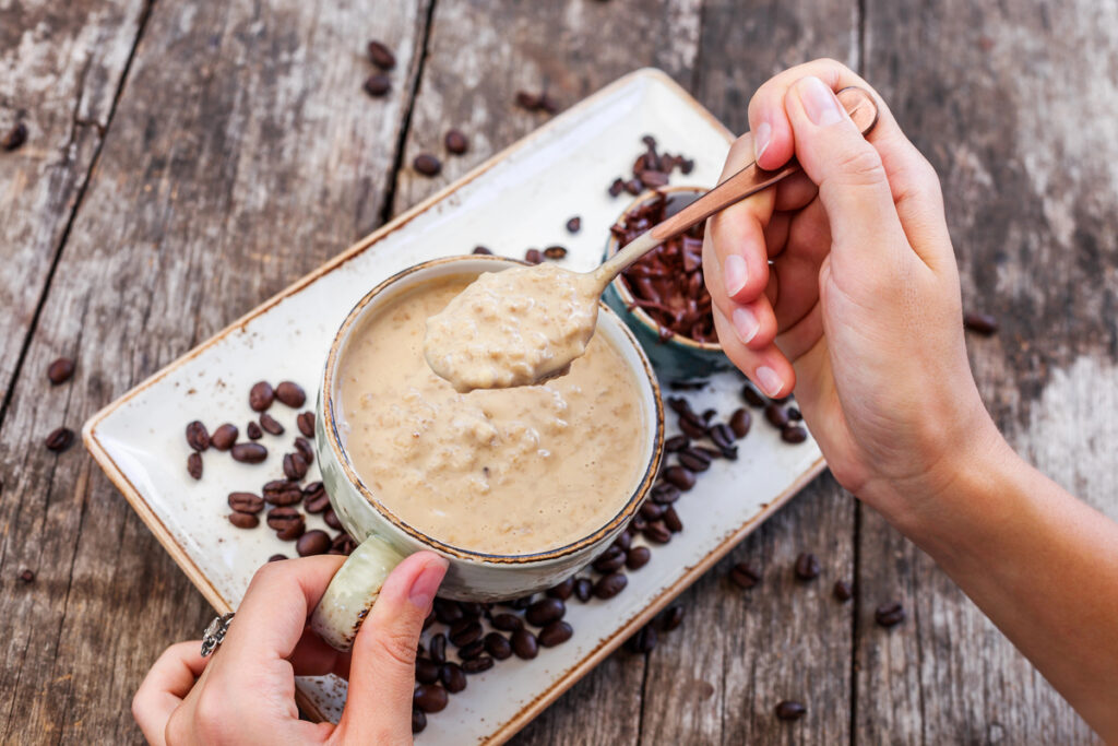 Woman eating oatmeal porridge with coffee and grated chocolate.