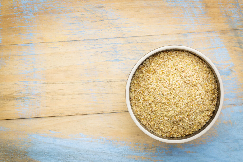 golden flaxseed meal - a ceramic bowl on grunge wood background with a copy space