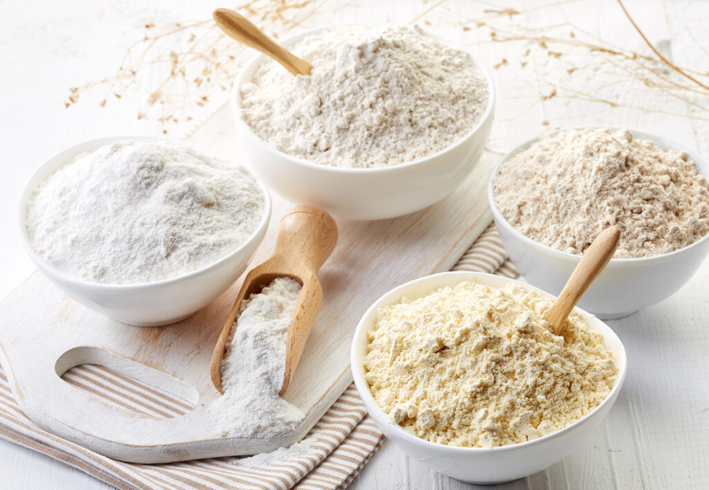 Bowls of various gluten free flour (chick peas, rice, buckwheat, amaranth seeds, almond) on white wooden background