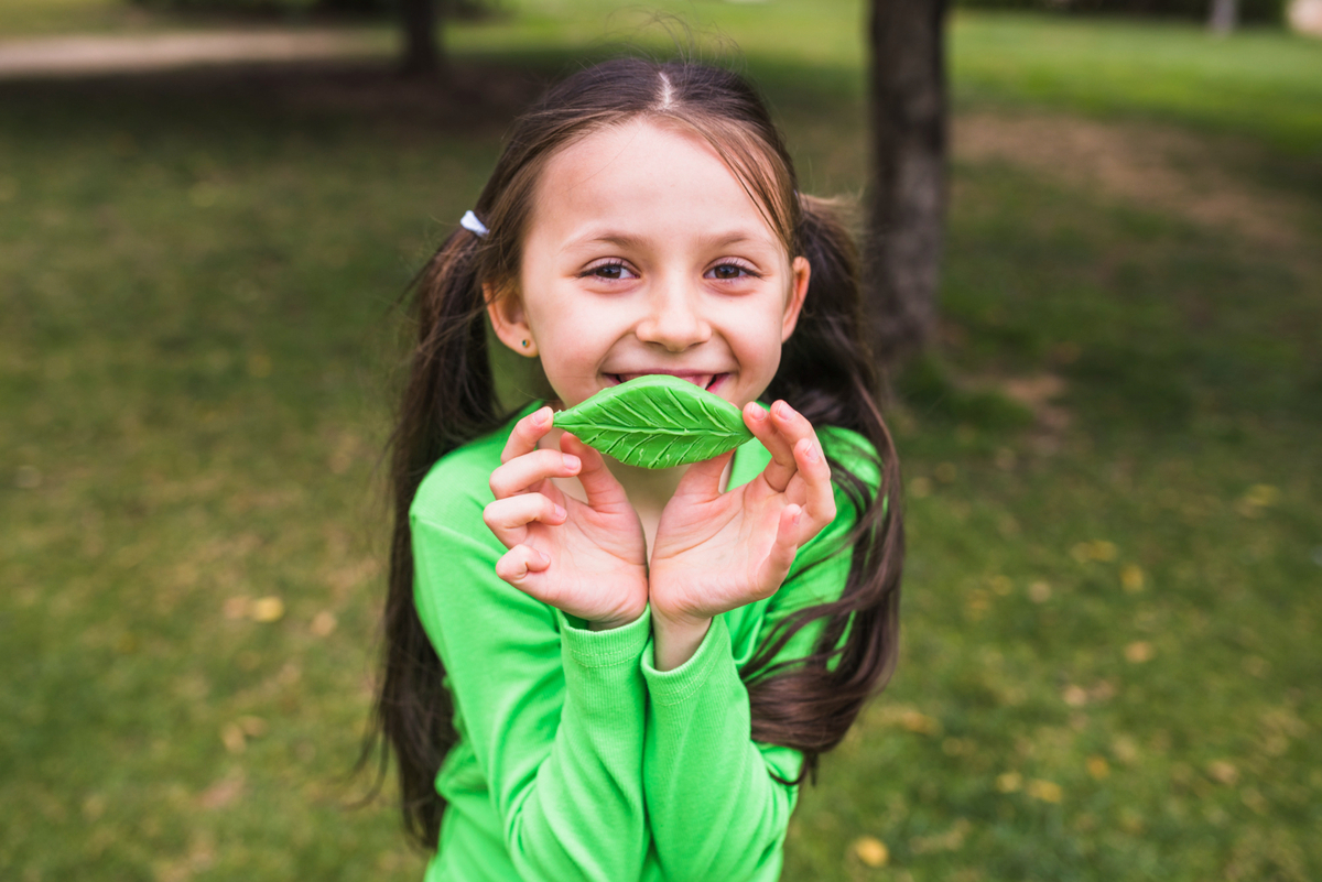 Cute smiling girl playing with fake clay leaf in park