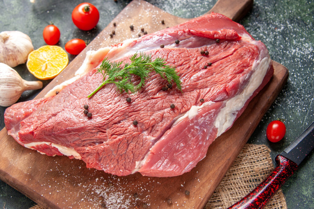 Front view of fresh raw red meat on wooden cutting board on nude color towel lemon garlic on mixed color background