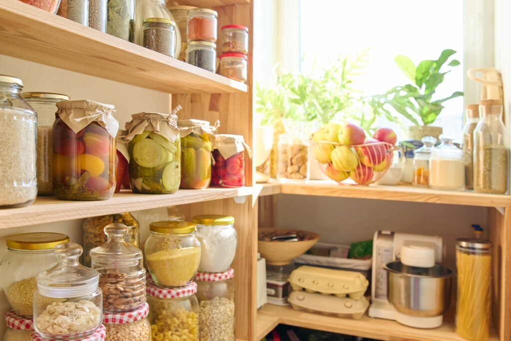 Storage of food in kitchen in pantry. Wooden cabinet with jars and containers, cereals, spices, paste, nuts, canned pickled fruits and vegetables, kitchen utensils. Eat at home, stock food concept