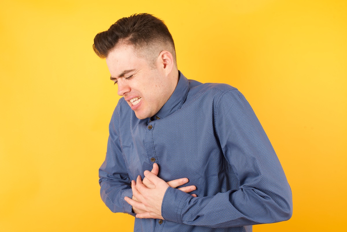 Beautiful young woman wearing red shirt over white isolated background with hand on stomach because nausea, painful disease feeling unwell. Ache concept.