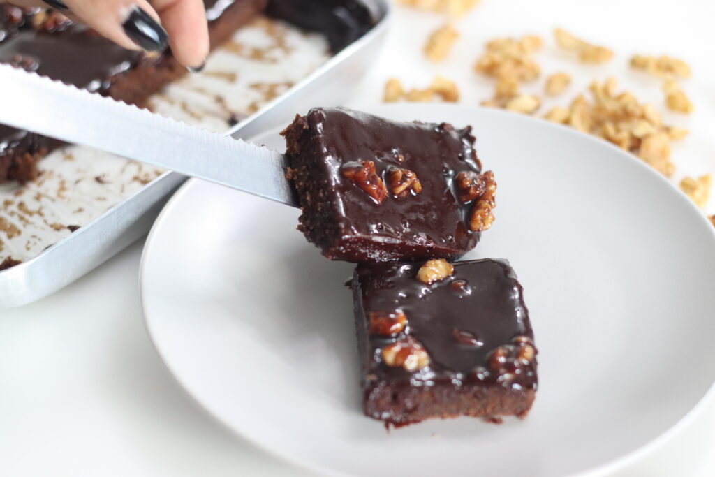 Slice of Texas Sheet Cake served on a plate. It is a large, thin chocolate cake topped with a rich chocolate walnut frosting. It's moist and fluffy, with a hint of cinnamon. A classic Southern dessert