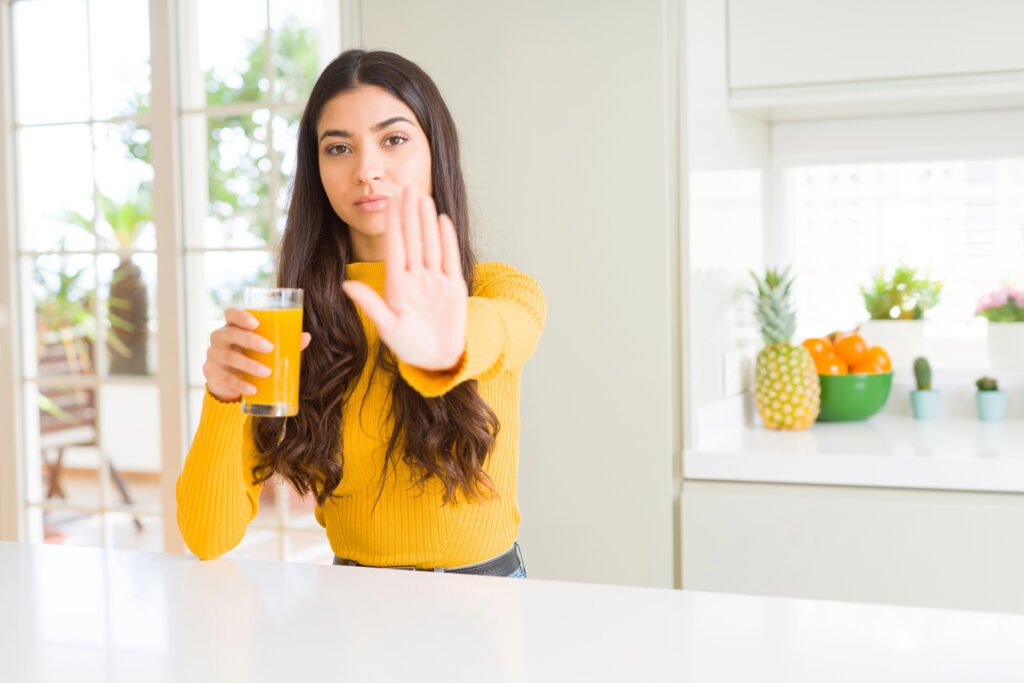 Young woman drinking a glass of fresh orange juice with open hand