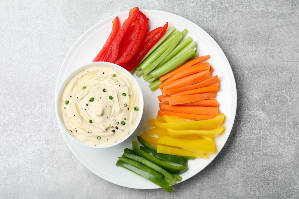 Fresh raw vegetable sticks and sauce on grey table, top view