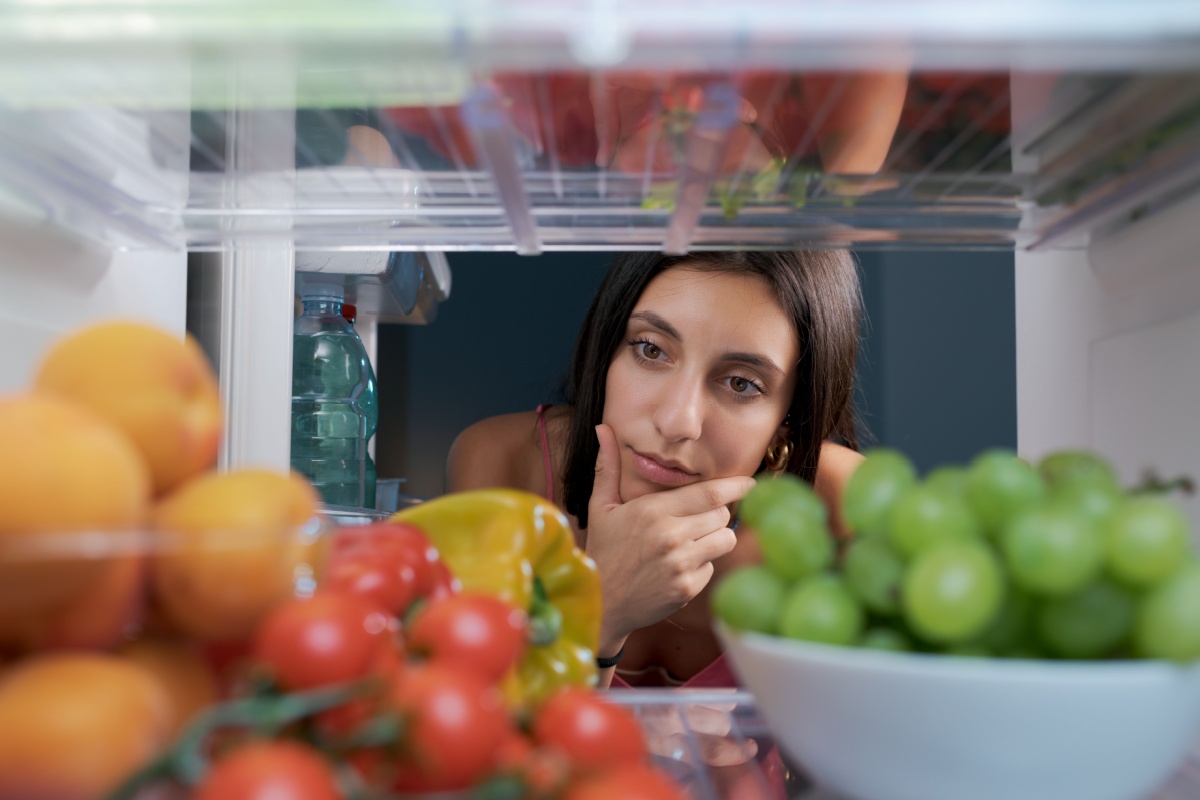 Woman looking in the fridge and thinking with hand on chin