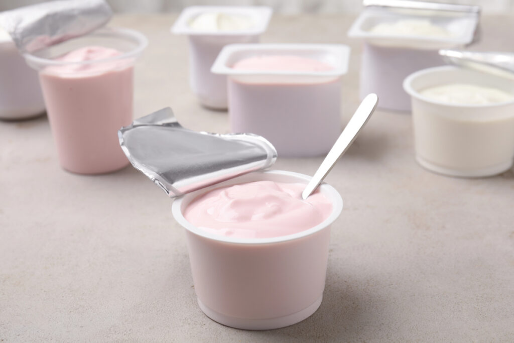 Plastic cup with fresh yogurt and spoon on grey table