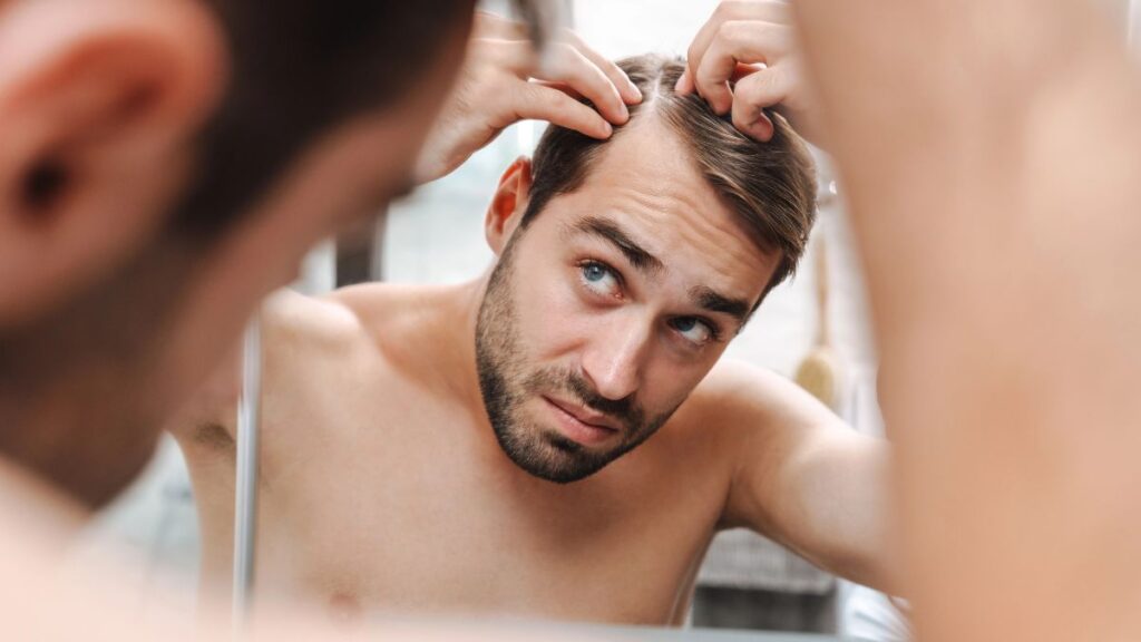 man looking at thin hair in mirror