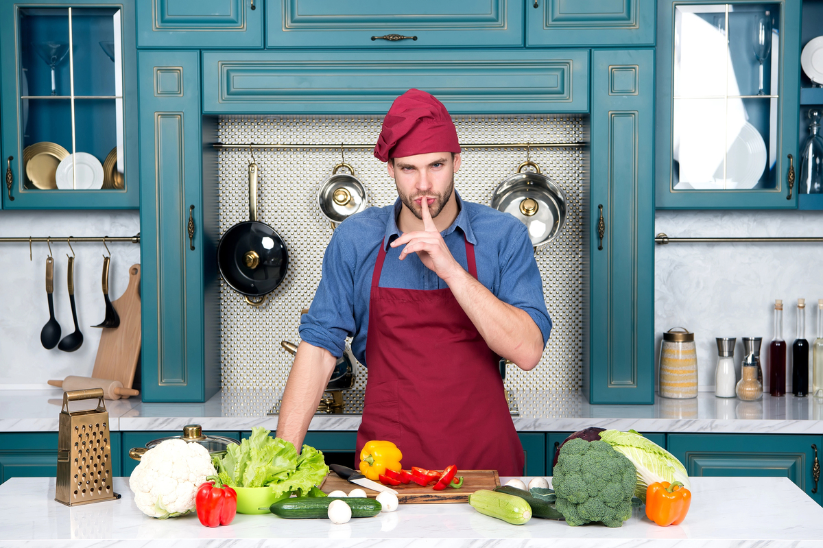 Chef with silence gesture finger at table with vegetables.