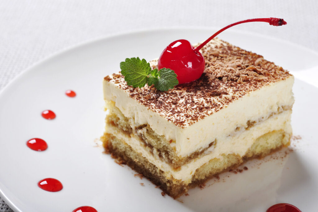 Tiramisu - Classical Dessert with  Coffee on white plate. Garnished with Cherry and Mint.