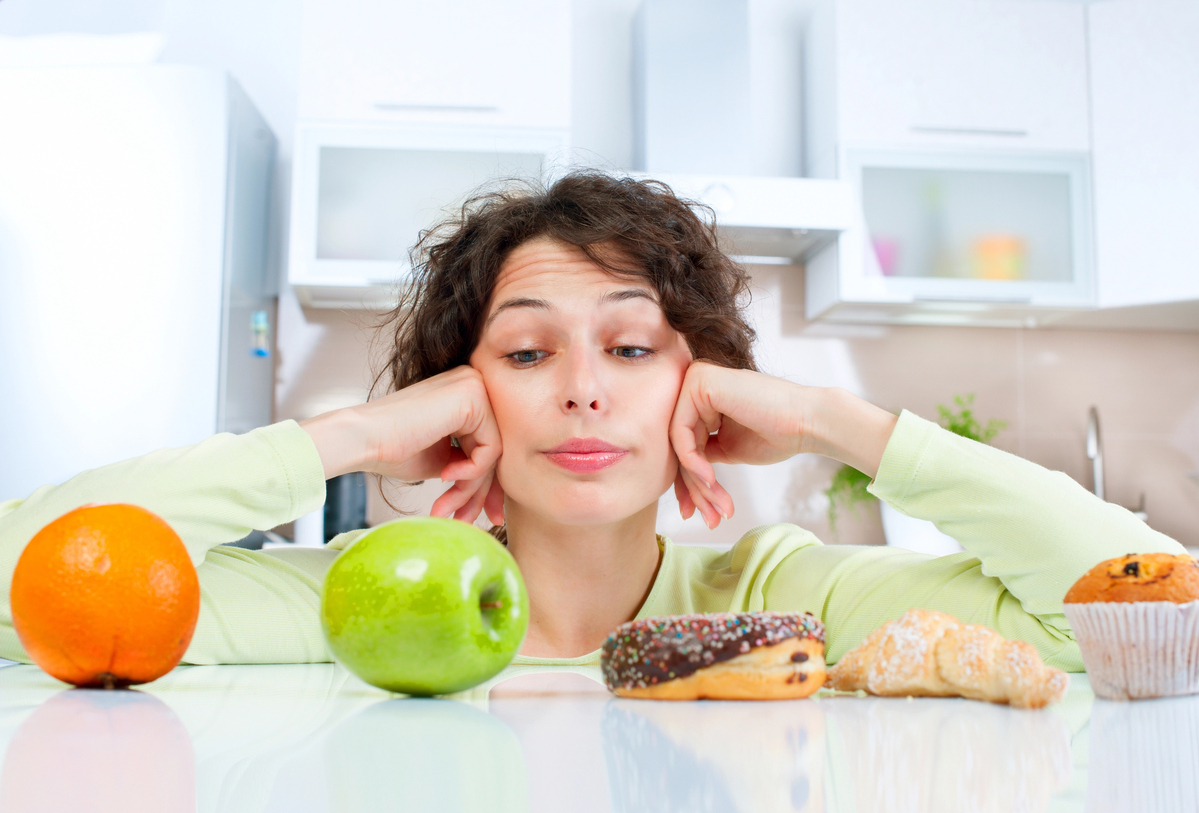 Dieting concept. Young Woman choosing between Fruits and Sweets