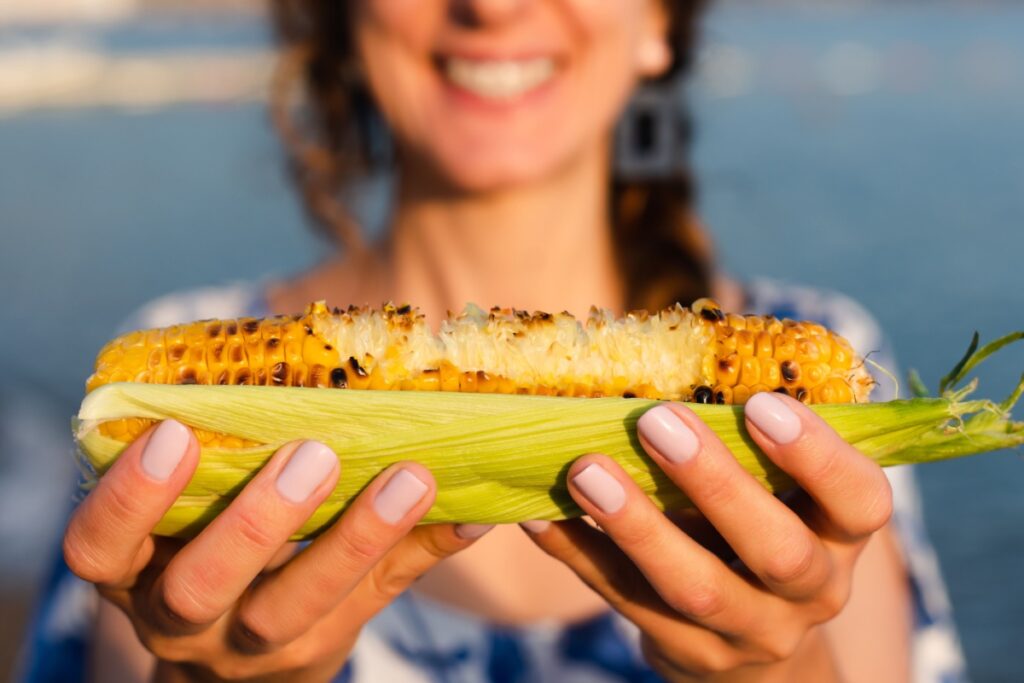 woman holding grilled corn on the cob