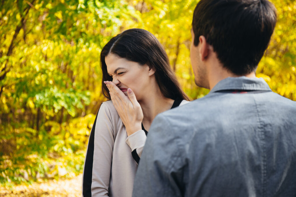 The man has bad breath. Woman turns away and closes her nose from the stench