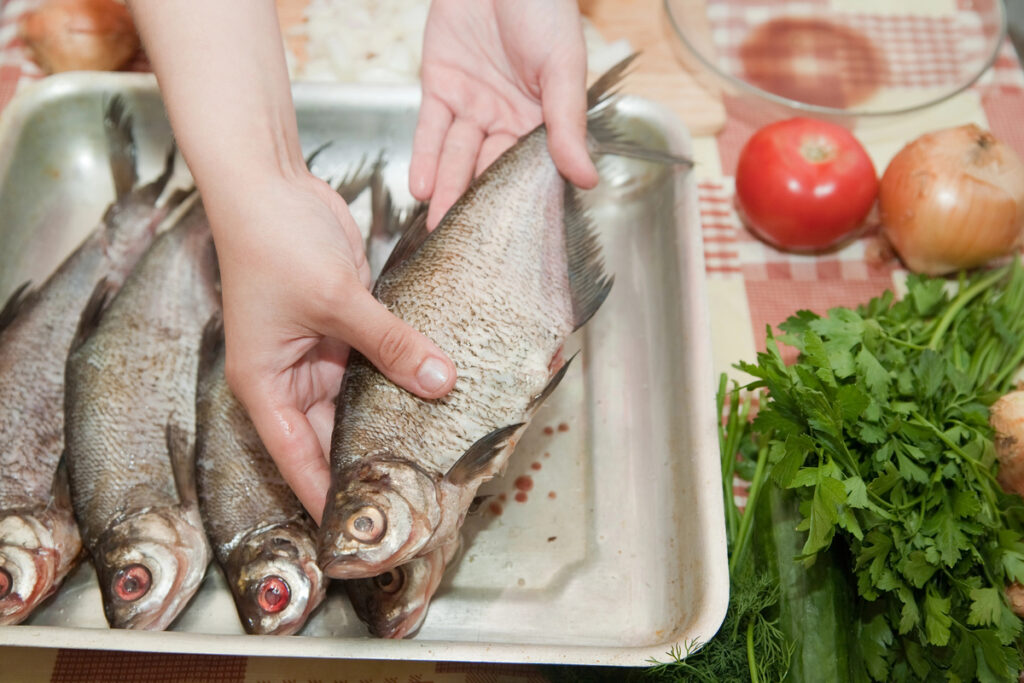 Young woman is cooking a fresh fish in kitchen