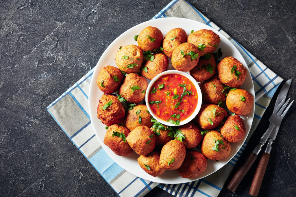 Plantain fritters Klako on a white platter served with hot sauce, vegan side dish, street food, african cuisine, view from above, flatlay, copy space