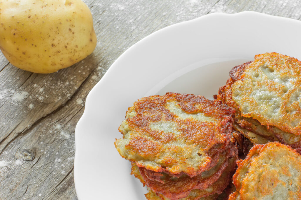 potato fritters with a golden crust in a white ceramic plate and a crude potato on the old gray burst board