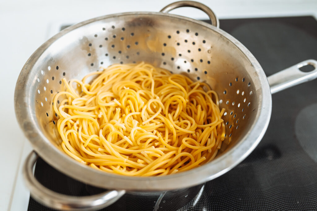 Boiled hot spaghetti in colander with steam