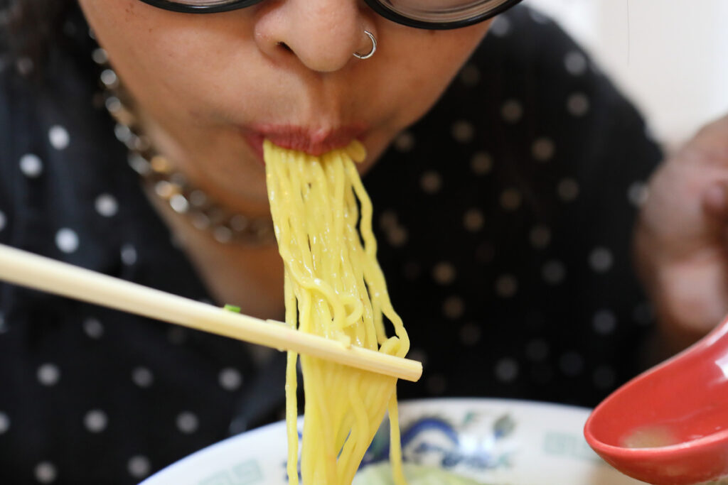 The Asian woman eating ramen in the restaurant.