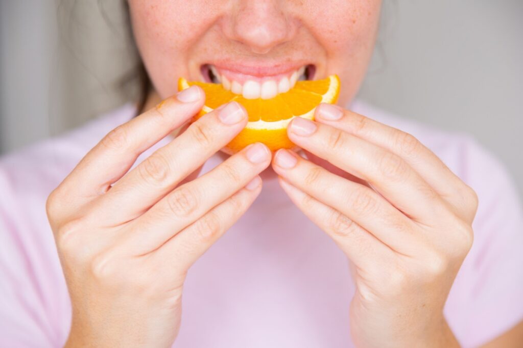 Young unrecognizable woman eating piece of orange