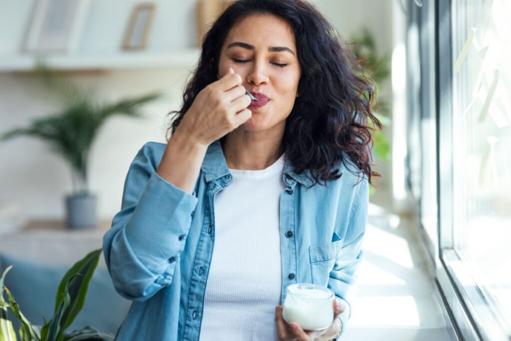  happy beautiful woman eating yogurt while standing in living room