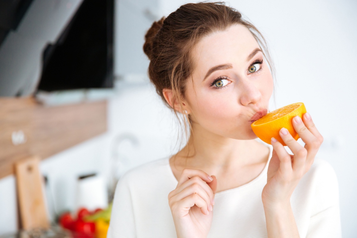 lovely young woman eating orange on the kitchen