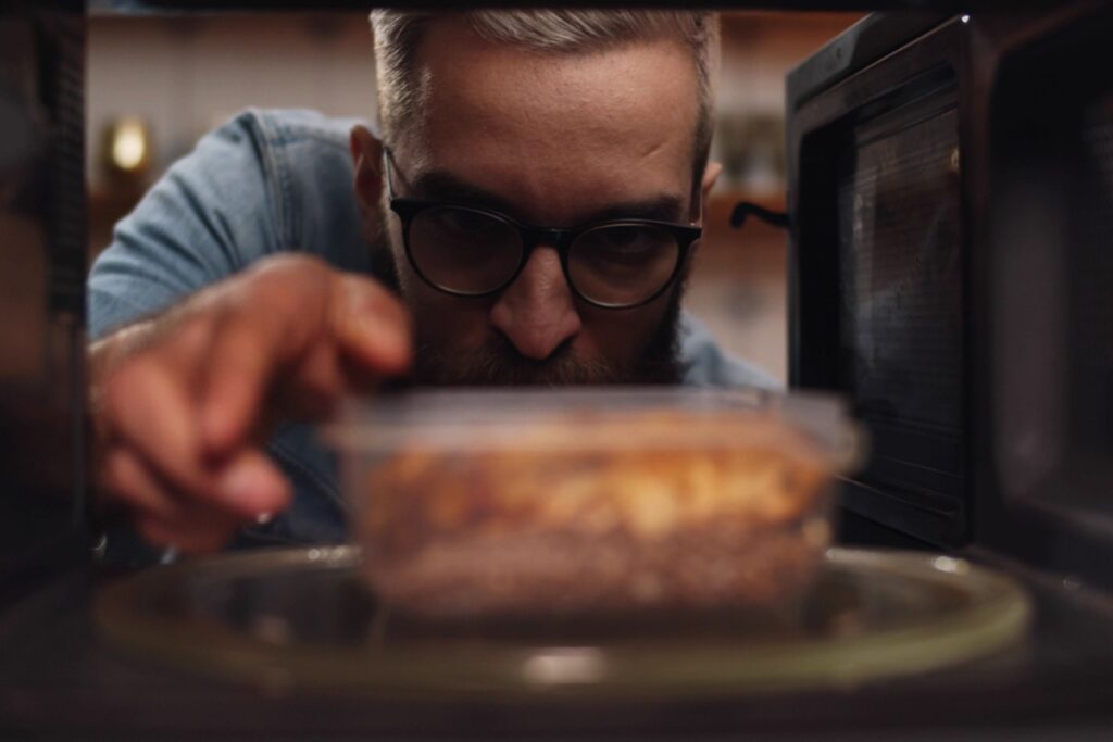 man microwaving leftovers in plastic Tupperware